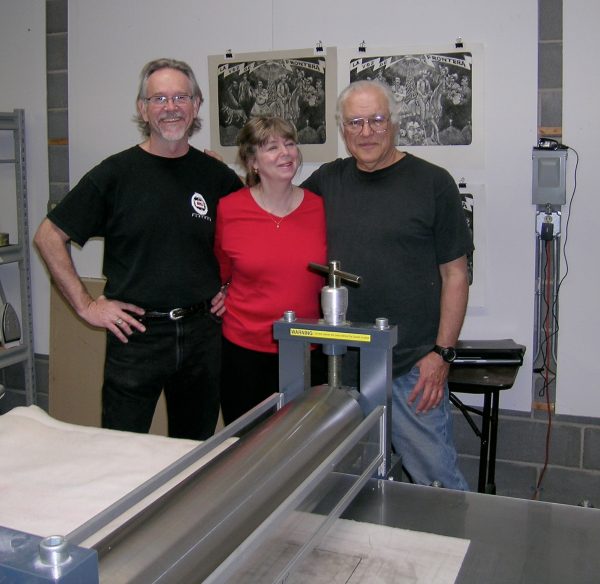 image of Flatbed press owners Mark Smith, Katherine Brimberry, and Lois Jiménez stand at the press